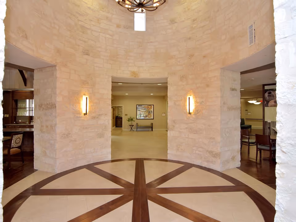 Round stone entryway with radial wood-and-tile floor inlay, wall sconces, and views into adjacent seating areas.