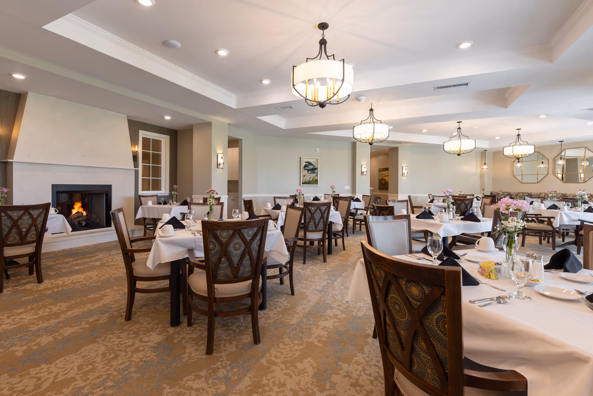 Spacious, well-lit dining room with elegantly set tables and a fireplace.