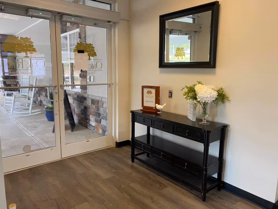 Entrance lobby with glass double doors, a black console table topped with flowers and a mirror above.