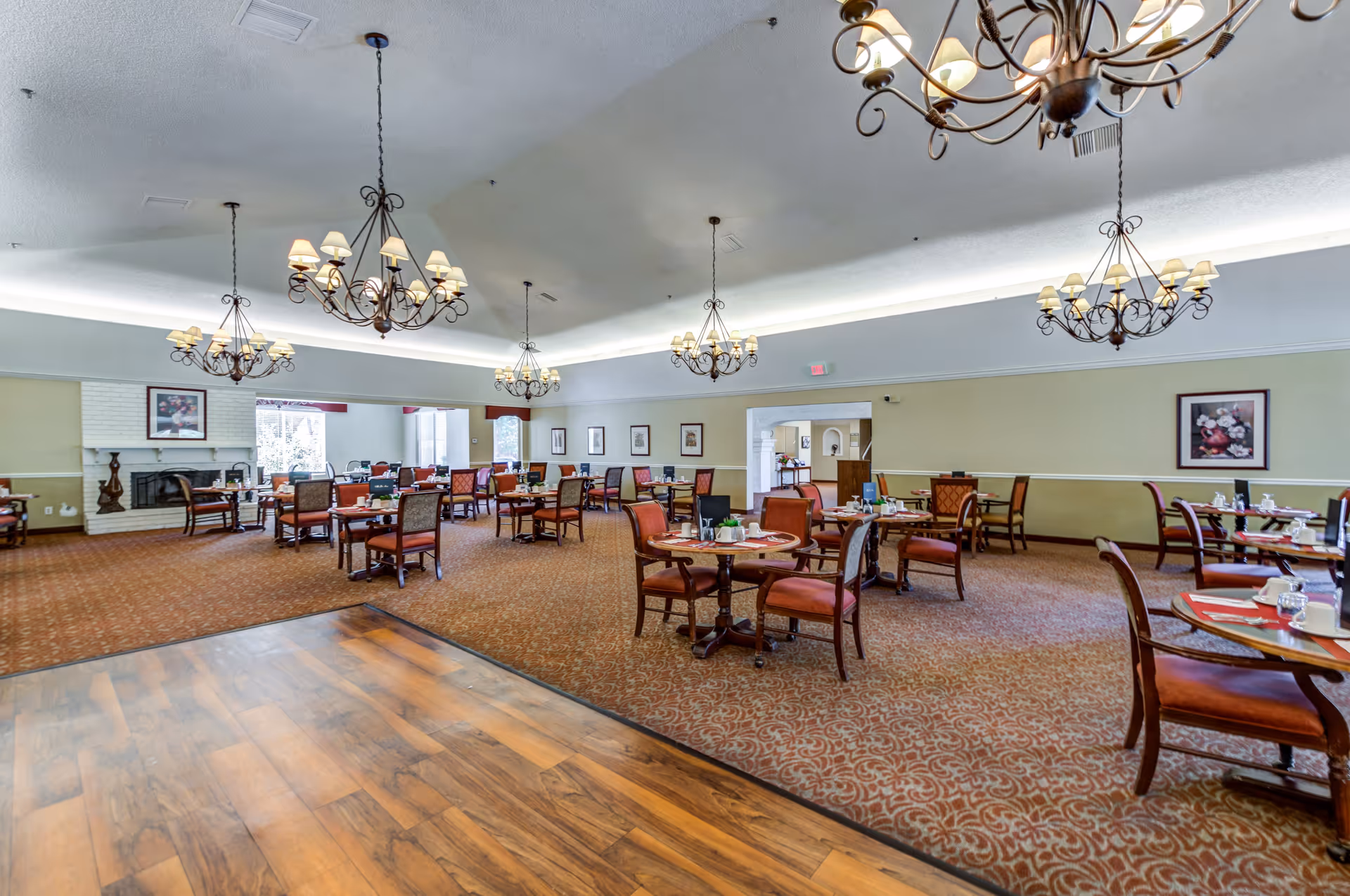 Spacious dining room with multiple round tables and chairs, ornate chandeliers, and a fireplace.