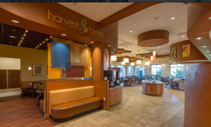 Interior view of a dining area named 'harvest bistro' with warm lighting, wooden and brown tones, cushioned bench seating, tables and chairs arranged for dining, and large windows letting in natural light.
