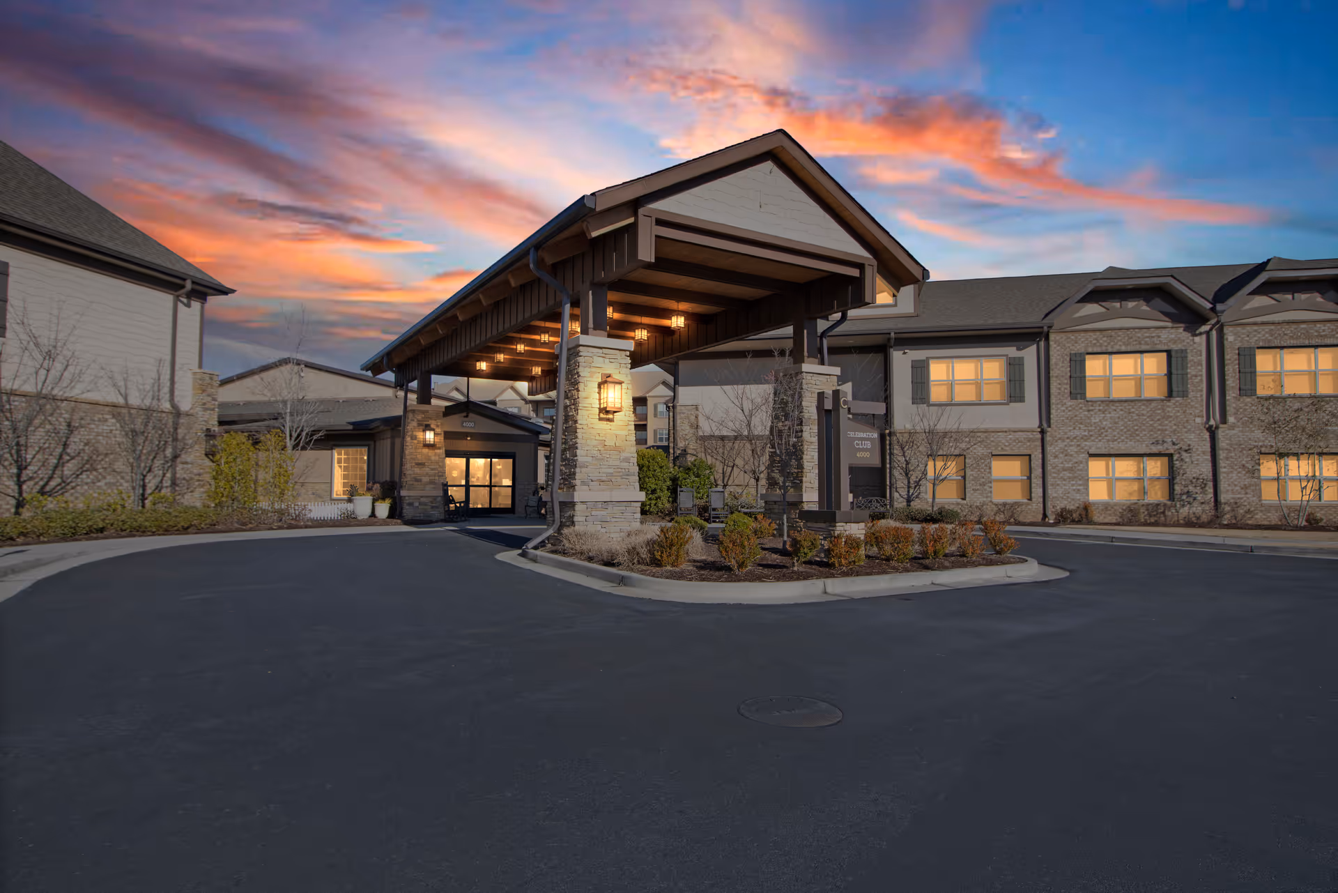 Front entrance of a senior living building with a covered porte-cochere and lit windows at sunset.