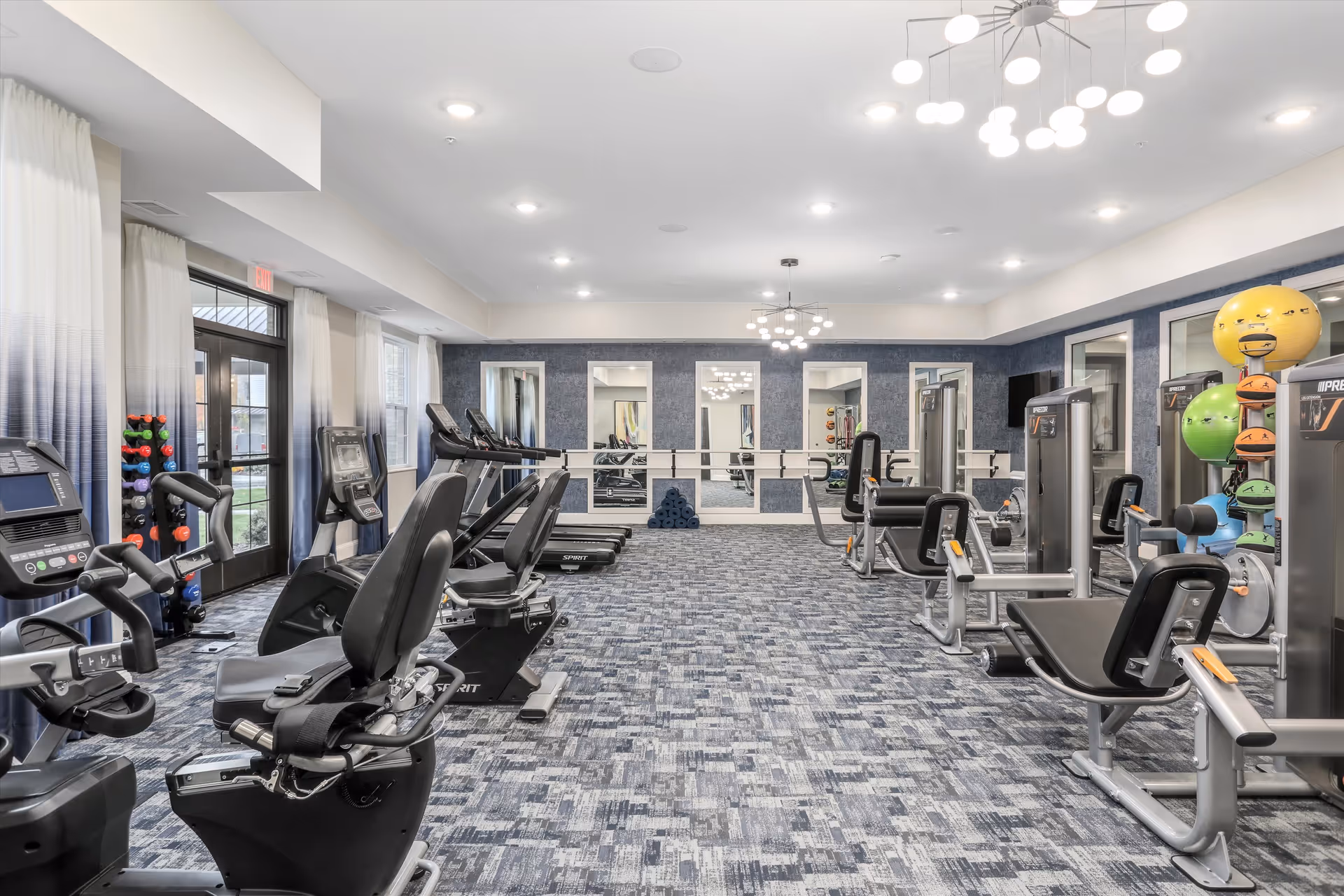 Bright modern fitness room with treadmills, recumbent bikes, weight machines and exercise balls.