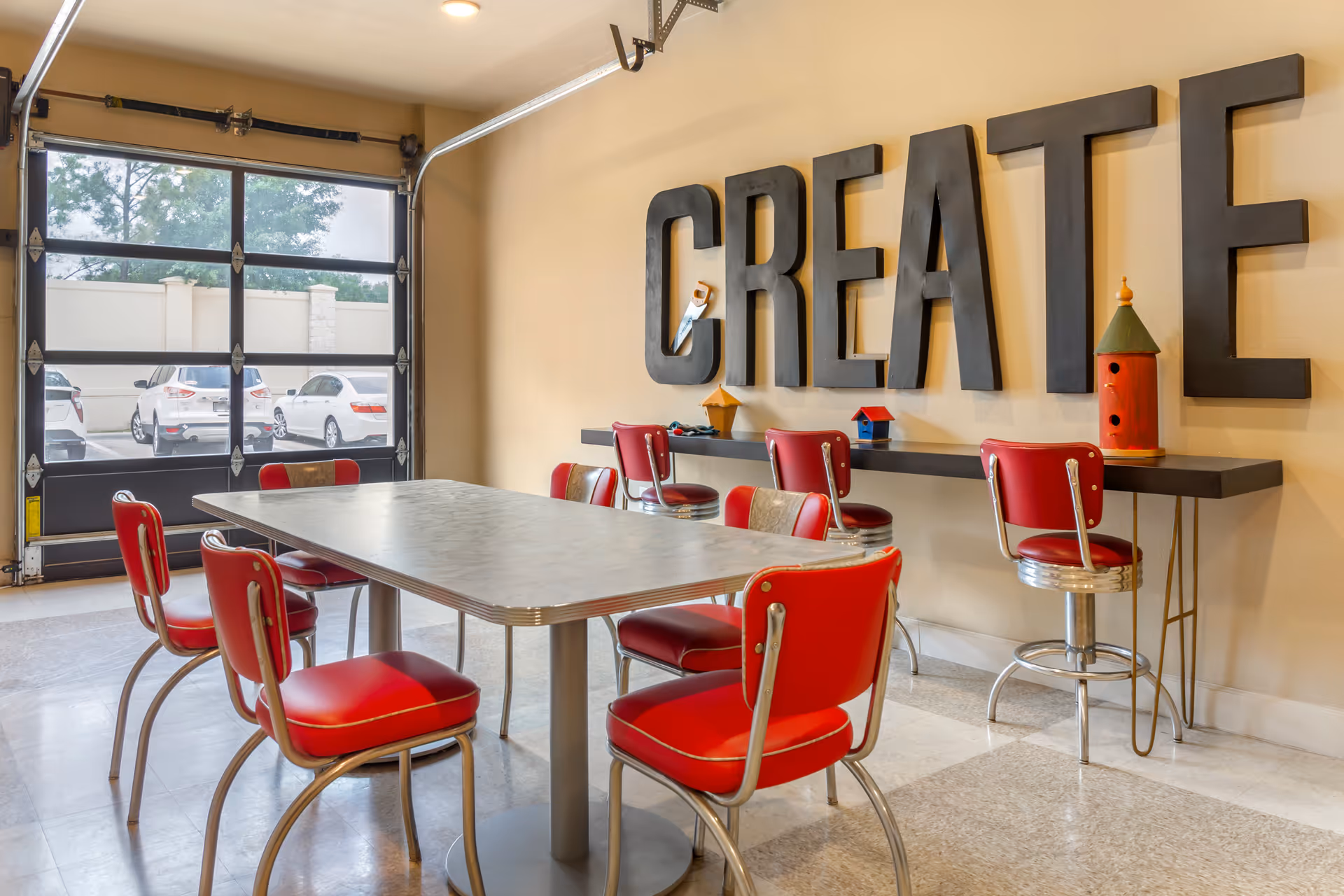A bright interior dining/activity room with a table surrounded by red retro chairs and large 'CREATE' letters on the wall.