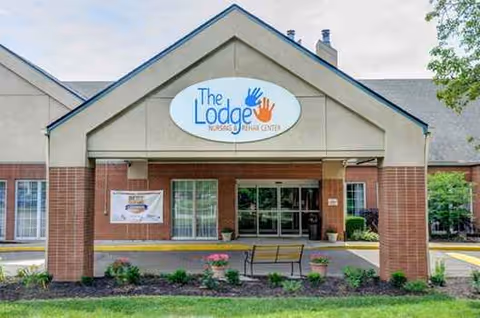 Exterior view of The Lodge Care Center entrance with a sign and landscaped front yard.