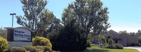 Exterior view of a nursing home with Kingston Nursing Center sign, trees and shrubs
