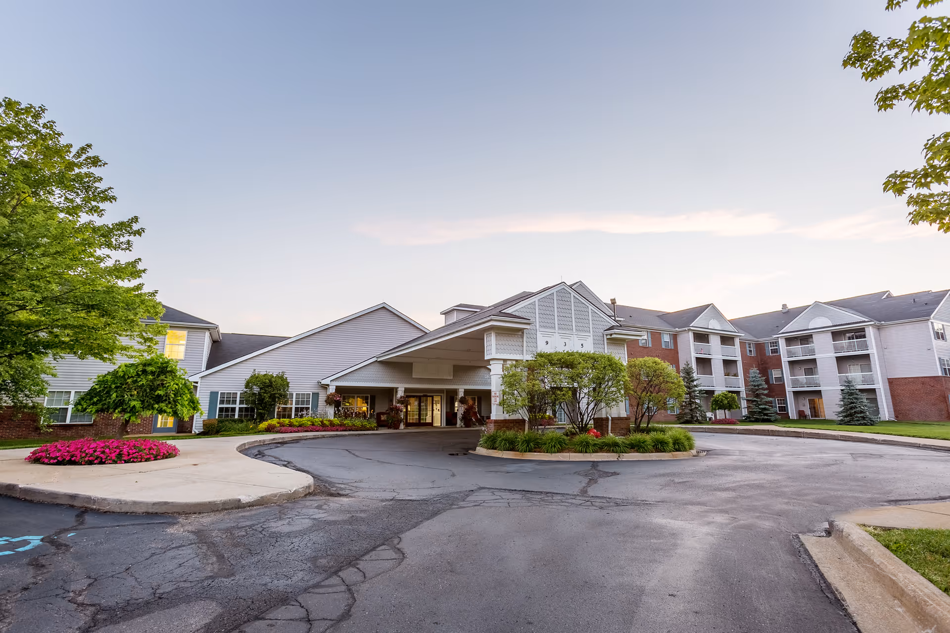 Front entrance and porte-cochère of a multi-story senior living building with balconies and a landscaped circular drive.