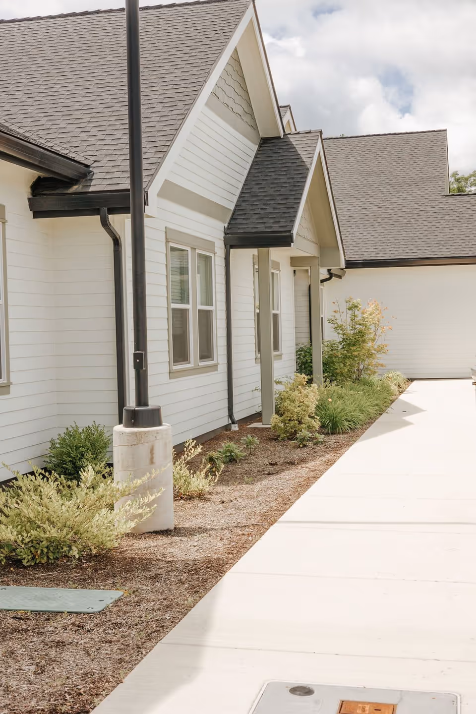 Exterior front of a single-story white building with gabled roofs, a sidewalk, lamp post, and landscaping.