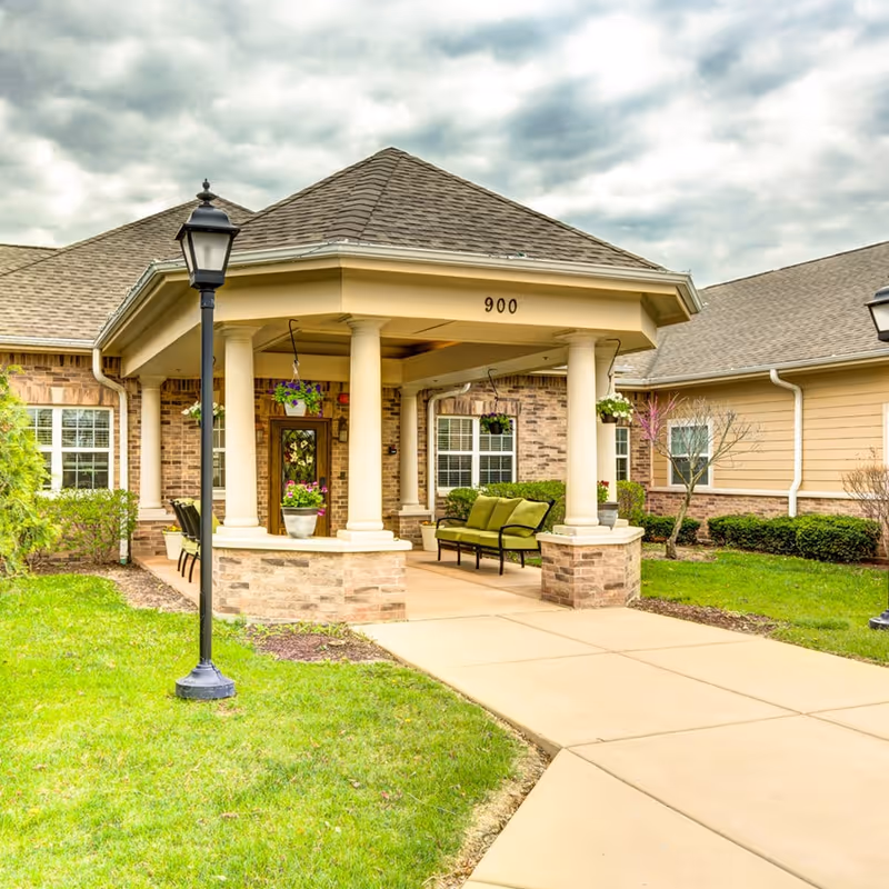 Front entrance of a senior living facility with a covered porch, columns, and a bench.