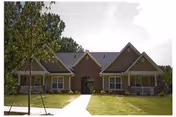 Front exterior view of a single-story residential building with a brick and siding facade, multiple gabled roofs, a central entrance, and a well-maintained lawn with a young tree and a concrete walkway leading to the door.