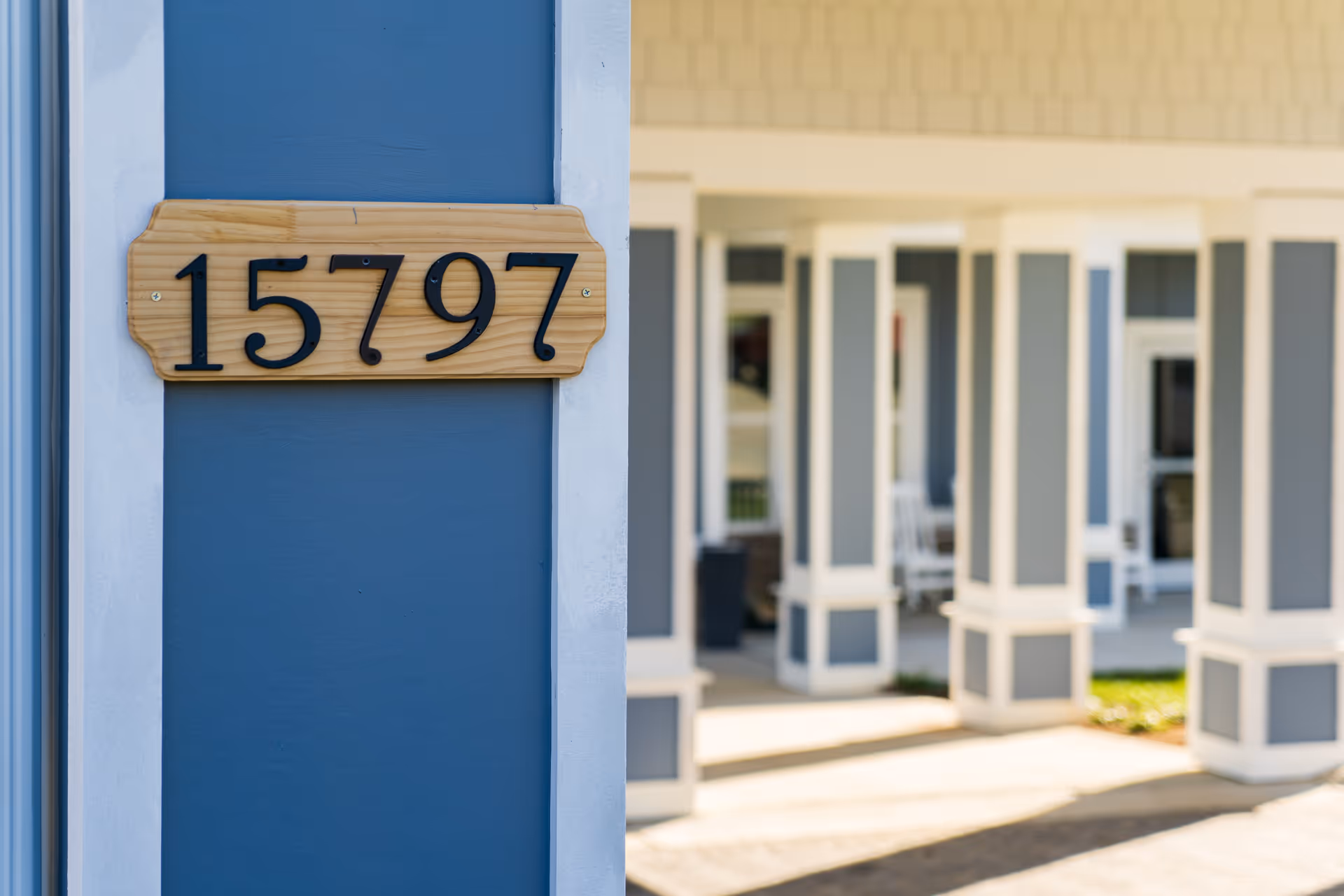 Wooden address plaque reading "15797" mounted on a blue exterior column with a covered porch and columns visible in the background.