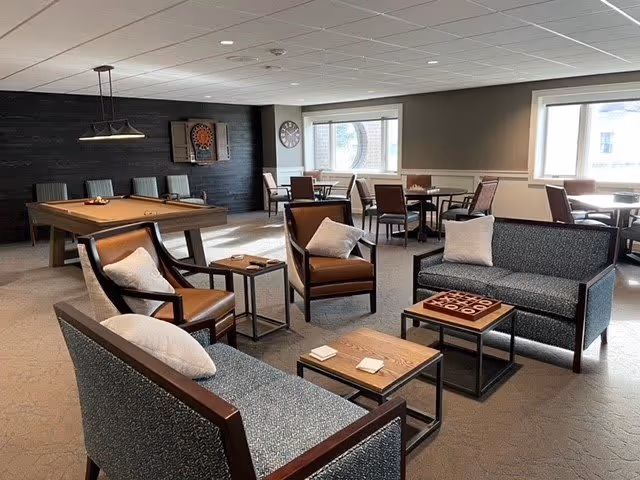 Communal lounge with sofas, armchairs, coffee tables, a pool table and dining tables by windows.