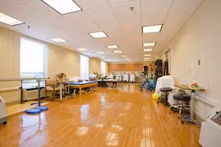 Bright rehab gym with tables, chairs, and exercise equipment in a long, polished interior.