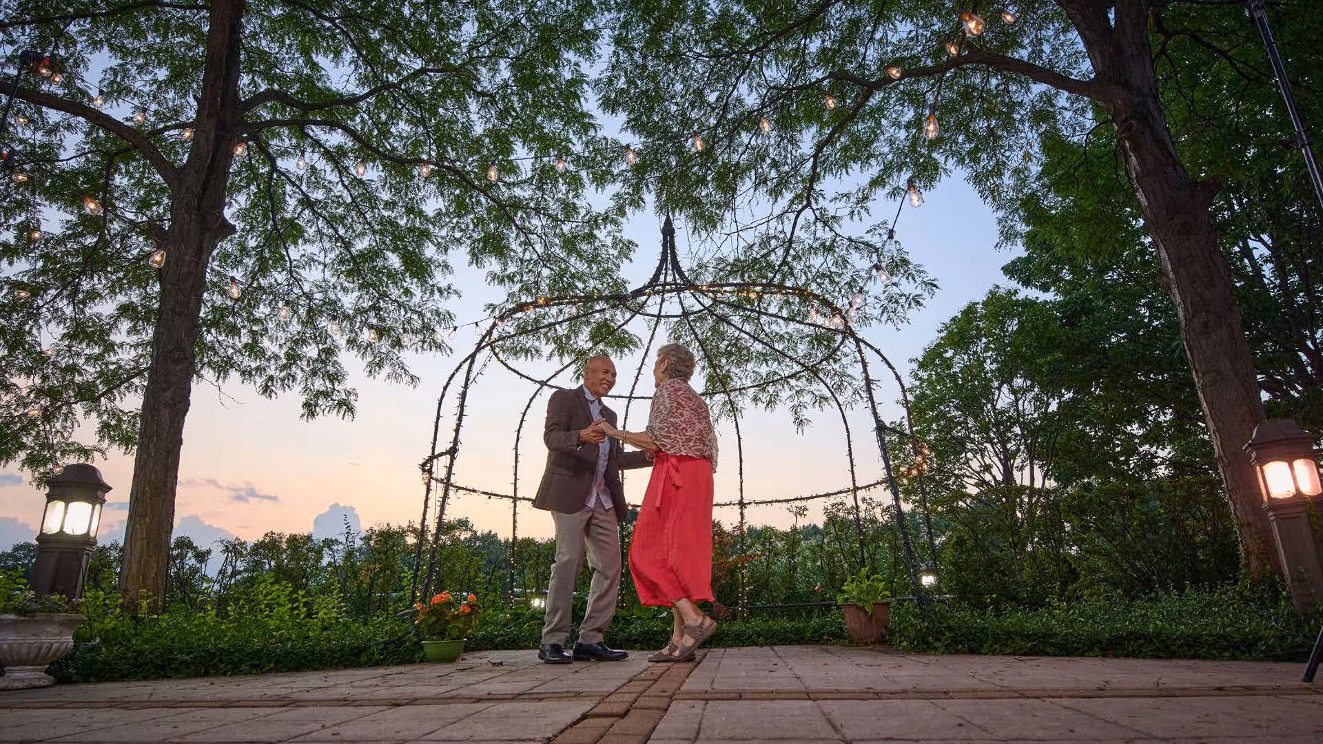 A couple dancing under a lit metal gazebo in a garden at dusk
