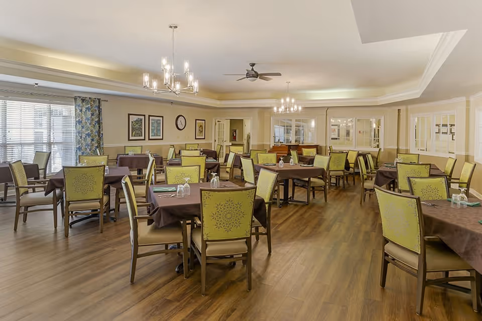 Well-lit dining room with multiple tables and green-upholstered chairs on a wood floor.