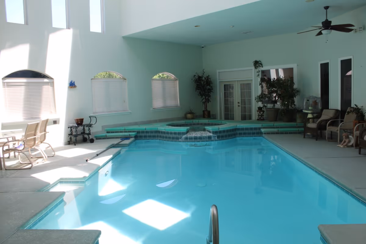 Indoor swimming pool with adjoining raised hot tub, lounge chairs and potted plants in a light-filled room.