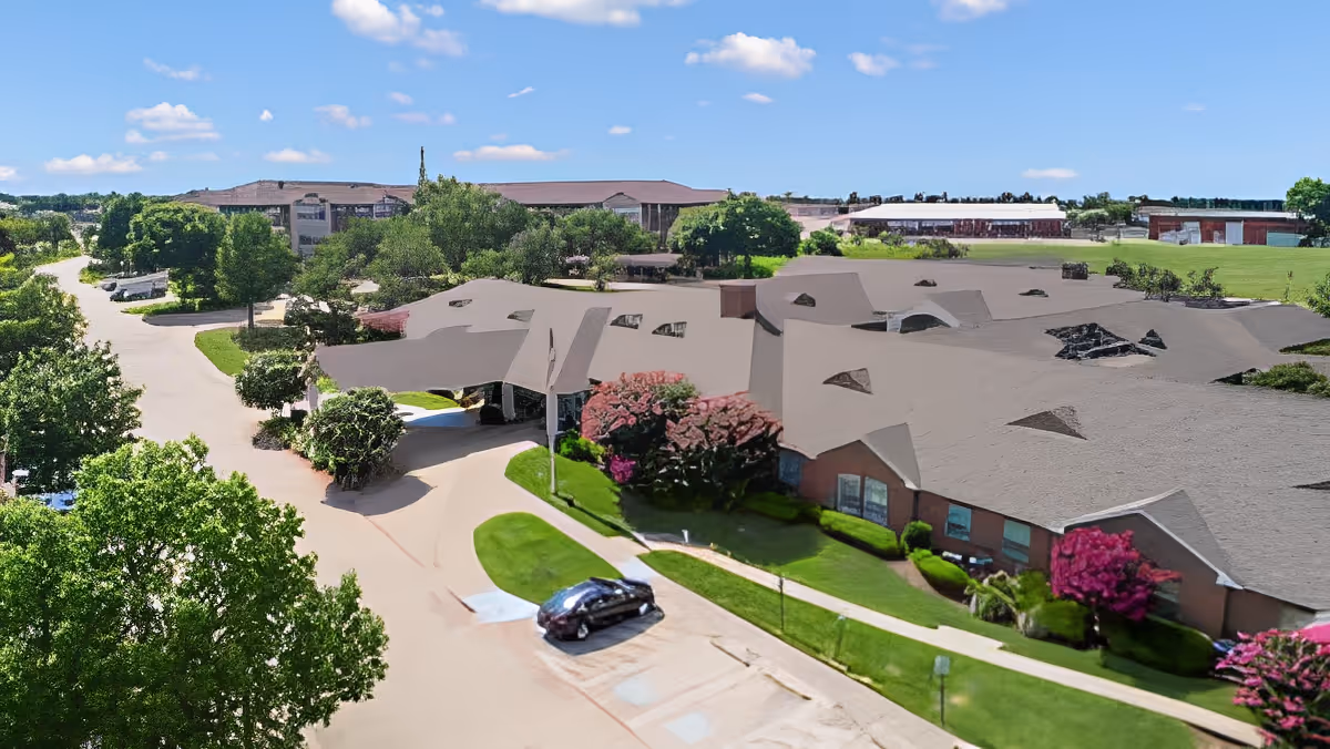 Aerial exterior view of a single-story brick senior living building with landscaped lawns, a drive-up canopy, and a parked car.