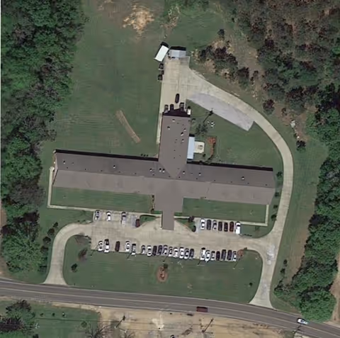Aerial view of a cross-shaped building with surrounding parking lots, driveways and grassy grounds.