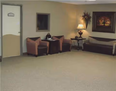 A spacious lounge with pink chairs, a sofa, lamps, wall art in a senior facility.