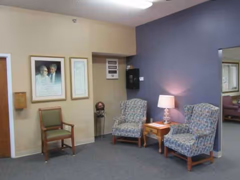 A waiting area with a blue accent wall, two patterned chairs, a lamp, and framed art.