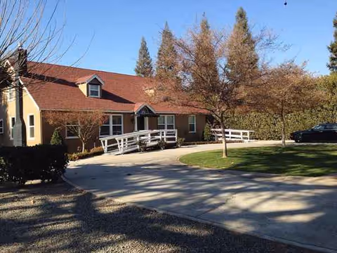 One-story senior living facility with curved driveway, white railing, and trees in front.