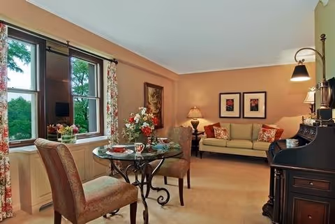 Cozy living room with a small round dining table by a window, a sofa, and framed artwork on the wall.