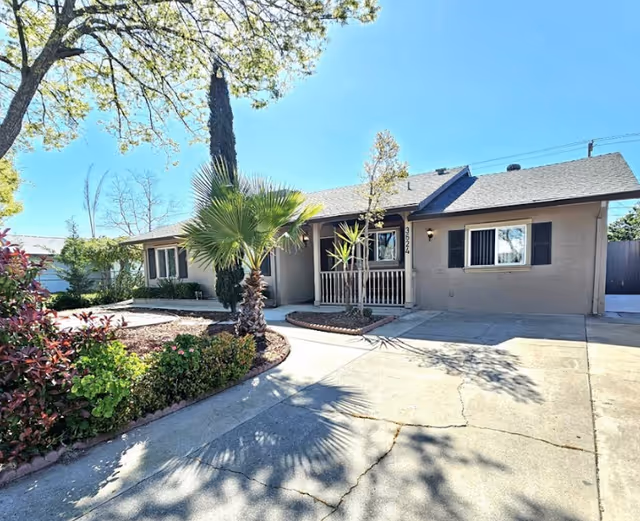 Single-story beige senior living facility exterior with a porch and landscaped driveway.