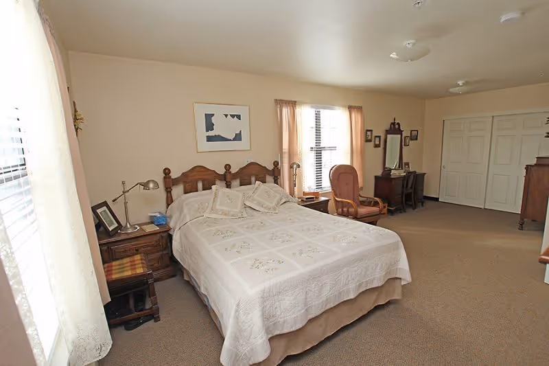 Spacious bedroom with a double bed, nightstands, armchair, dresser, desk, and large closet.