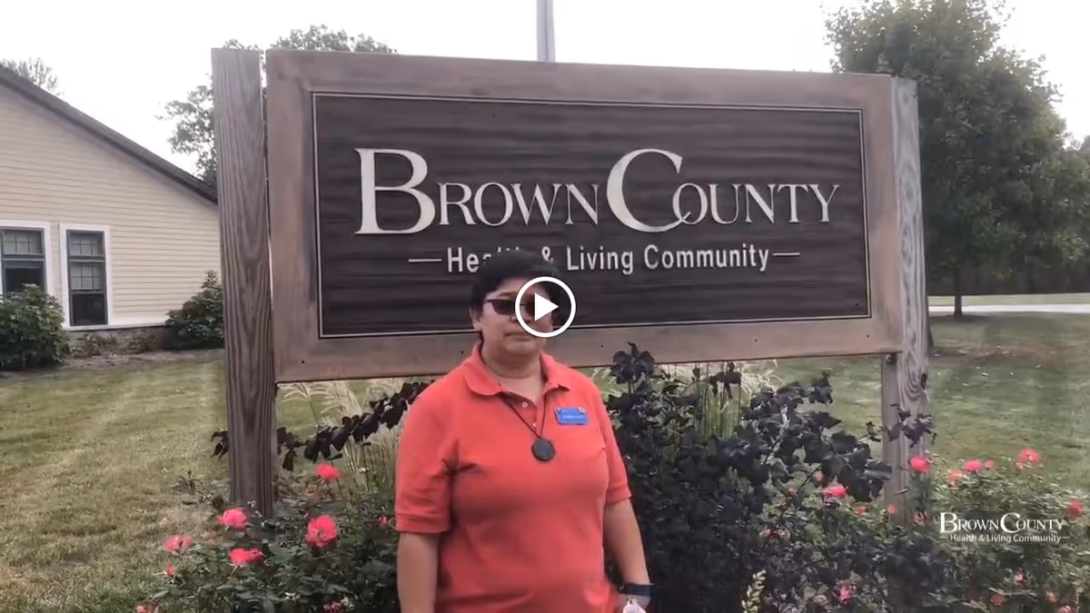 A person stands in front of a large wooden sign reading 'Brown County Health & Living Community' on the facility lawn.