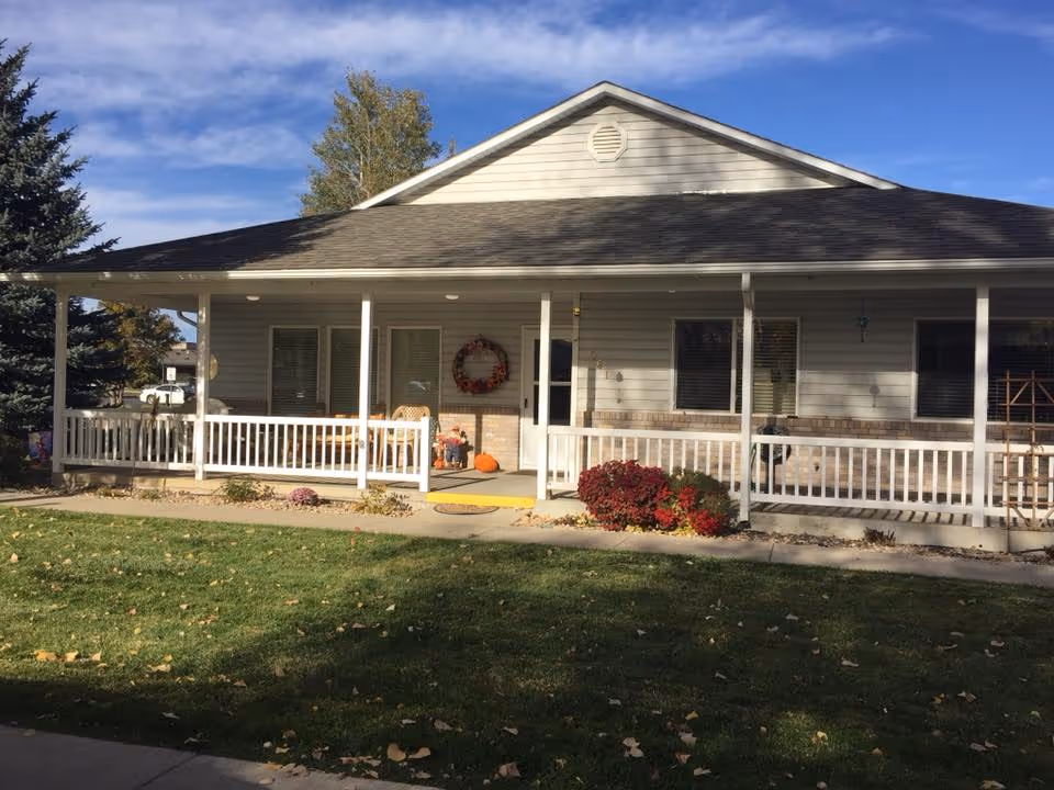 Front exterior of a single-story building with a covered porch, white railing, lawn, and autumn decorations.
