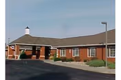Red brick senior living facility exterior with parking lot and landscaped shrubs.