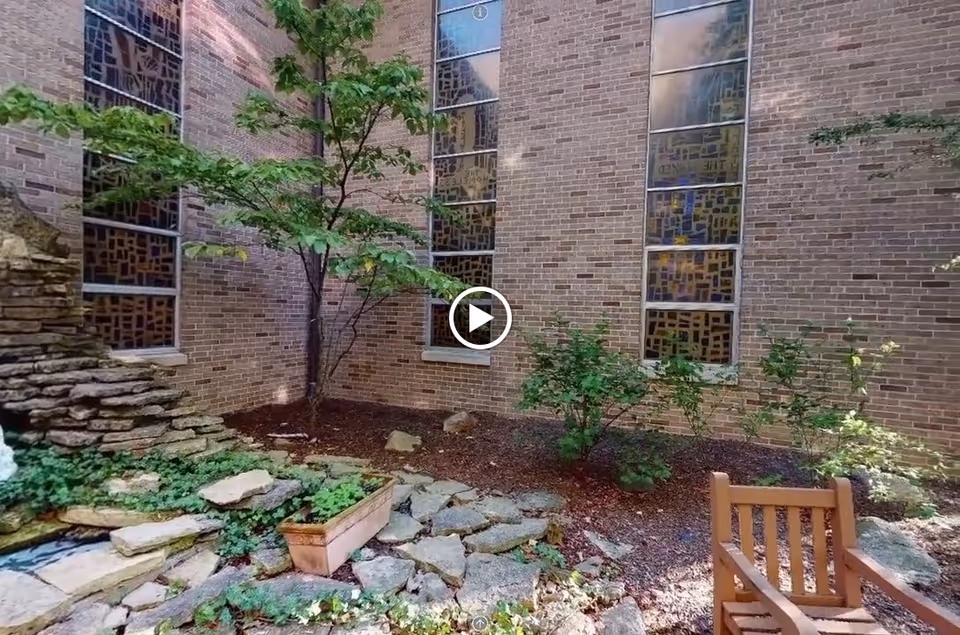 Small enclosed brick courtyard with a tree, planter, rock water feature, and a wooden bench.