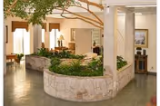 Interior lobby with a central stone planter containing greenery and a small tree, surrounded by seating and lamps.
