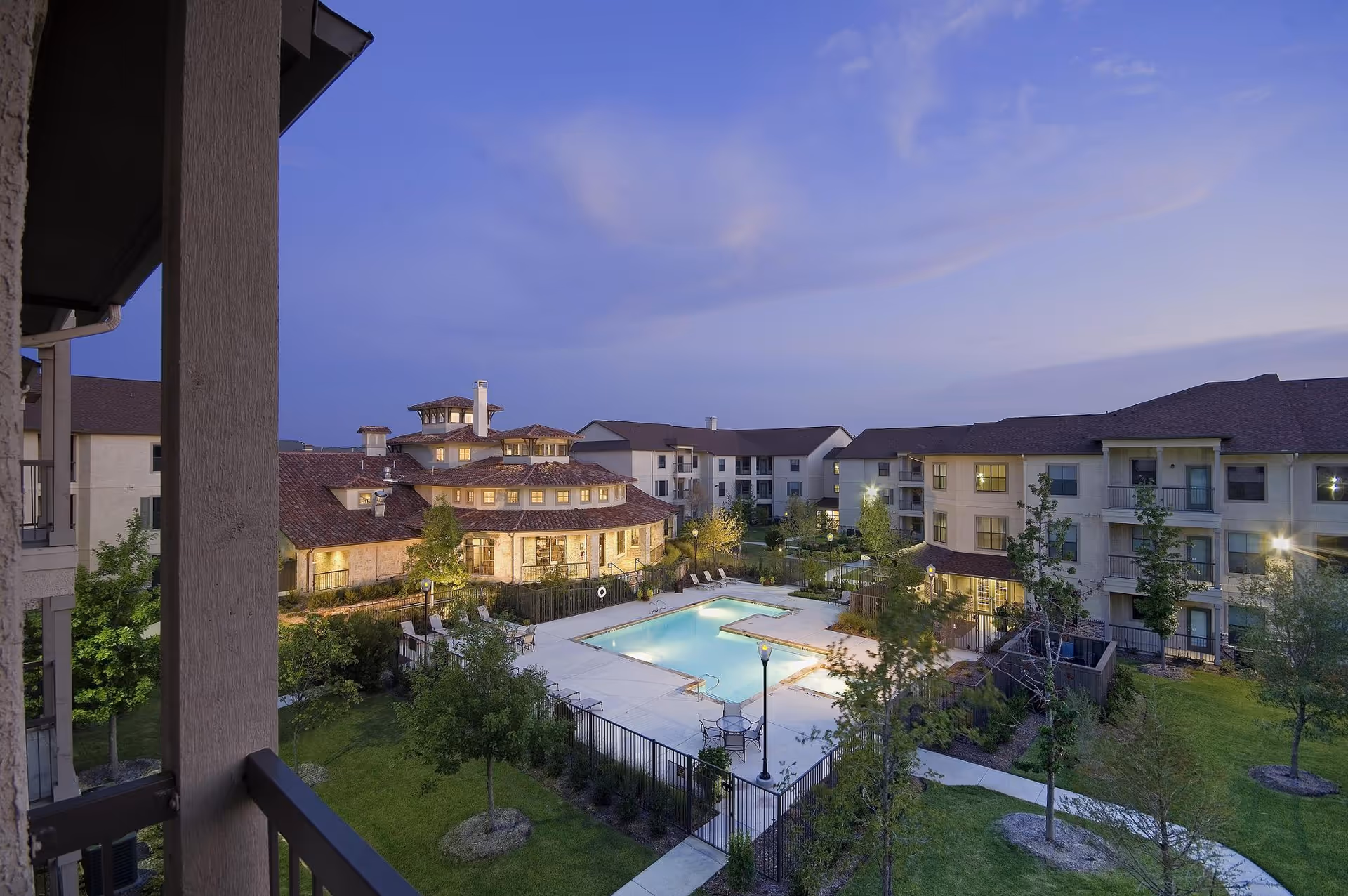 Evening view of a senior living courtyard featuring a lit outdoor swimming pool surrounded by multi-story buildings.