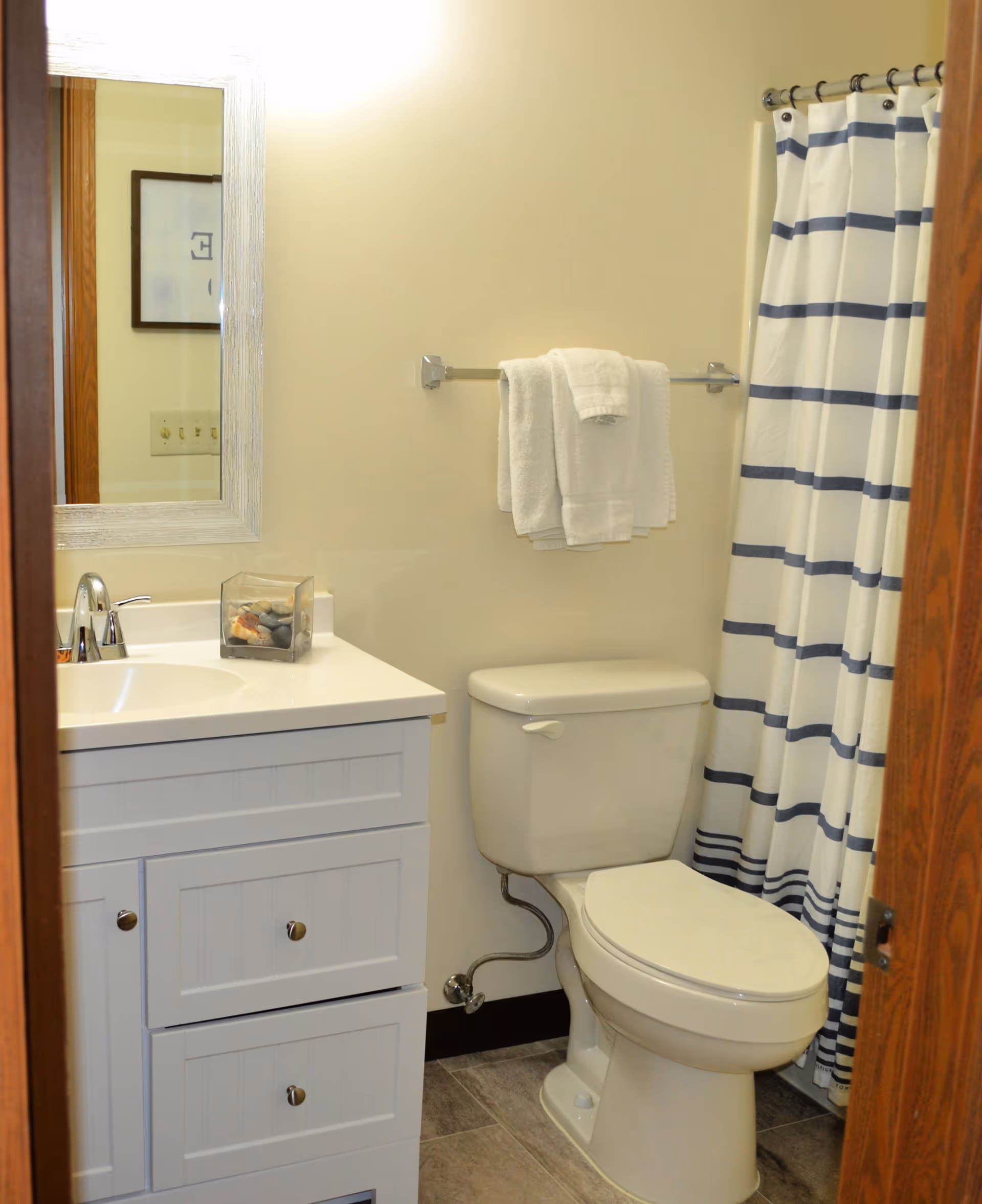 Small bathroom with a white vanity and sink, a toilet, towel rack, and a blue-striped shower curtain.