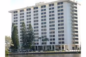 Exterior view of a multi-story residential building named De Soto Towers Inc, with several rows of windows and surrounded by tall trees near a body of water.