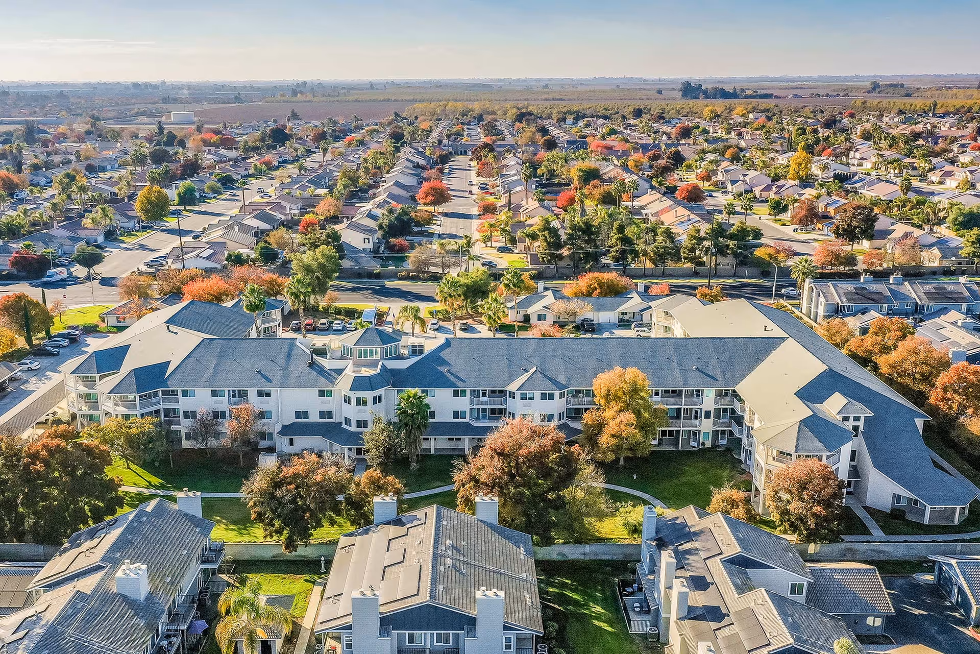 Aerial view of a large multi-wing senior living complex with landscaped lawns and trees surrounded by a suburban neighborhood.