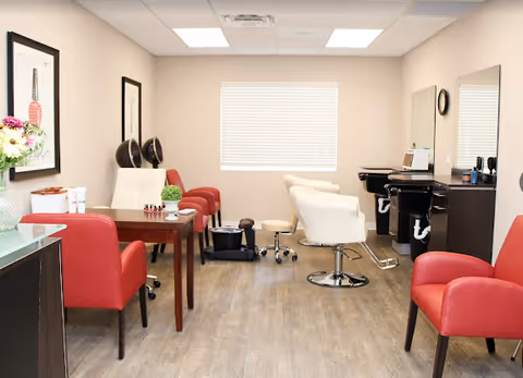 Well-lit salon-style room with red and white chairs, a manicure table, hairdressing stations and pedicure equipment.