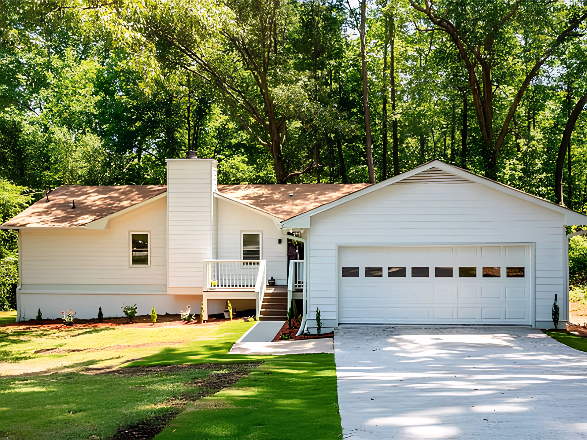 Front exterior of a white single-story house with an attached two-car garage, small front porch, driveway, and trees in the background.