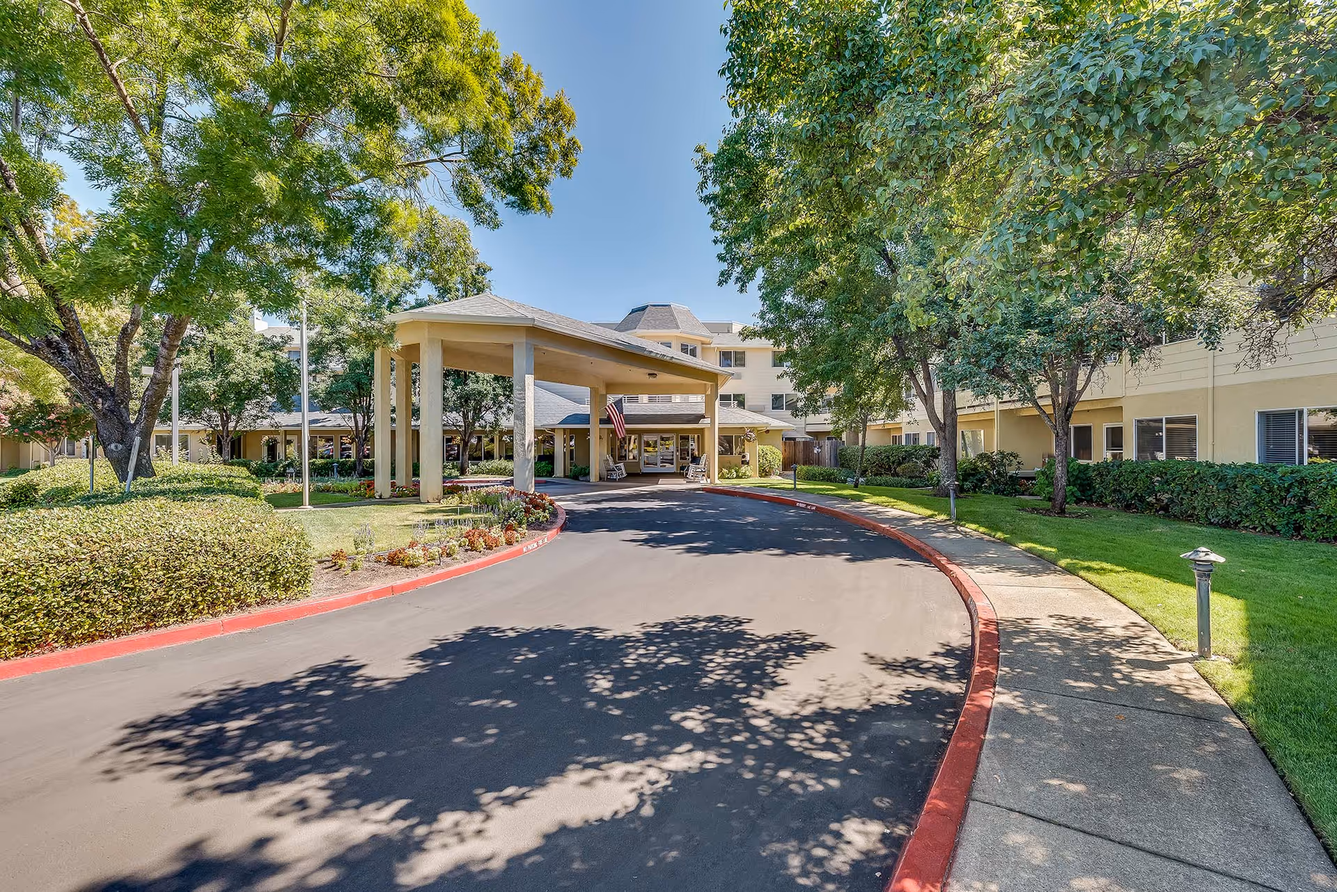 Front entrance of a senior living facility with a covered porte-cochere, circular driveway, and landscaped trees.