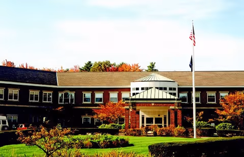 Front exterior of a two-story senior living building with a covered entrance, flagpole, and landscaped lawn.
