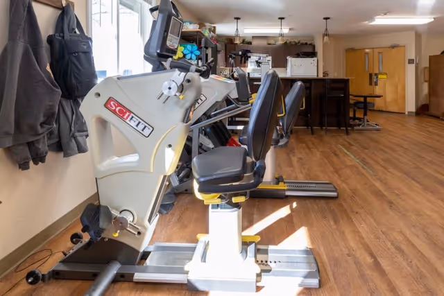 Recumbent exercise bikes and fitness equipment arranged in a wood‑floored communal activity room.