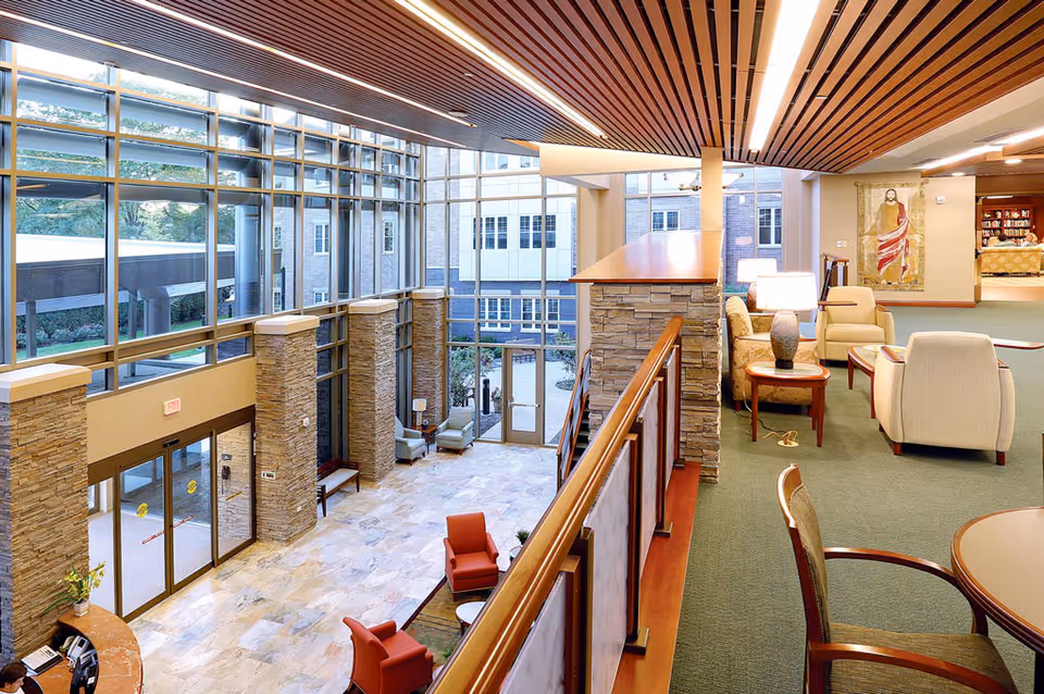 Bright two-story lobby and lounge with floor-to-ceiling windows, seating areas, and a mezzanine overlooking the entrance.