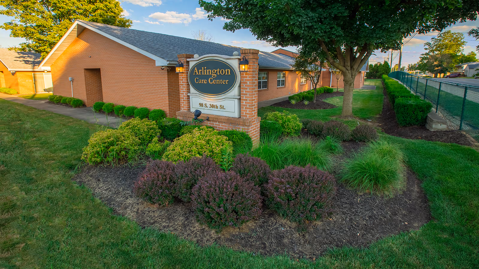 Brick single-story building and landscaped front lawn with a sign reading "Arlington Care Center."