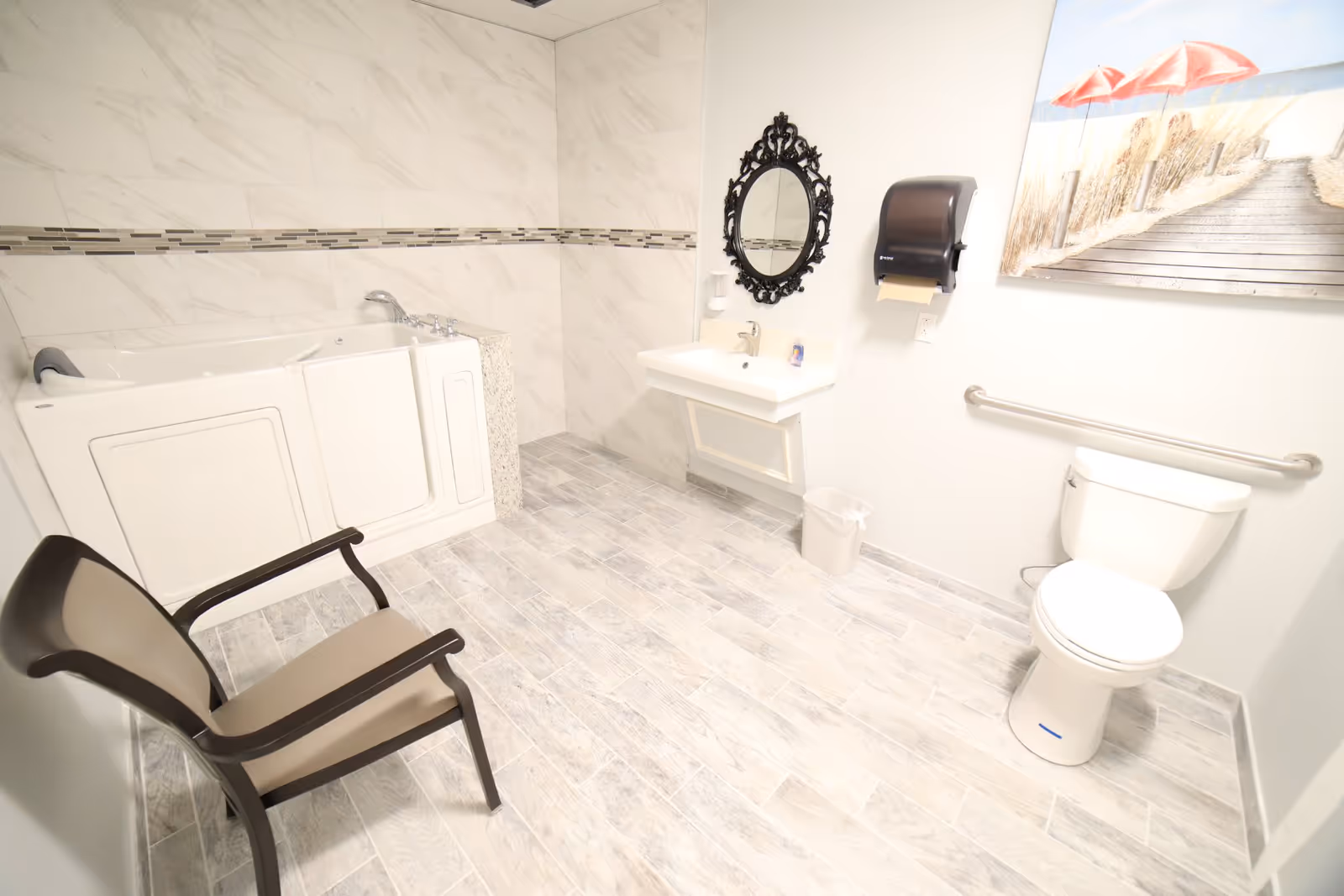 Accessible bathroom with a walk-in tub, toilet, sink, chair and wall art.