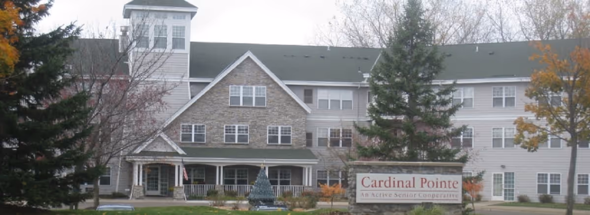 Front exterior of the Cardinal Pointe senior living building with a landscaped entrance and stone sign.