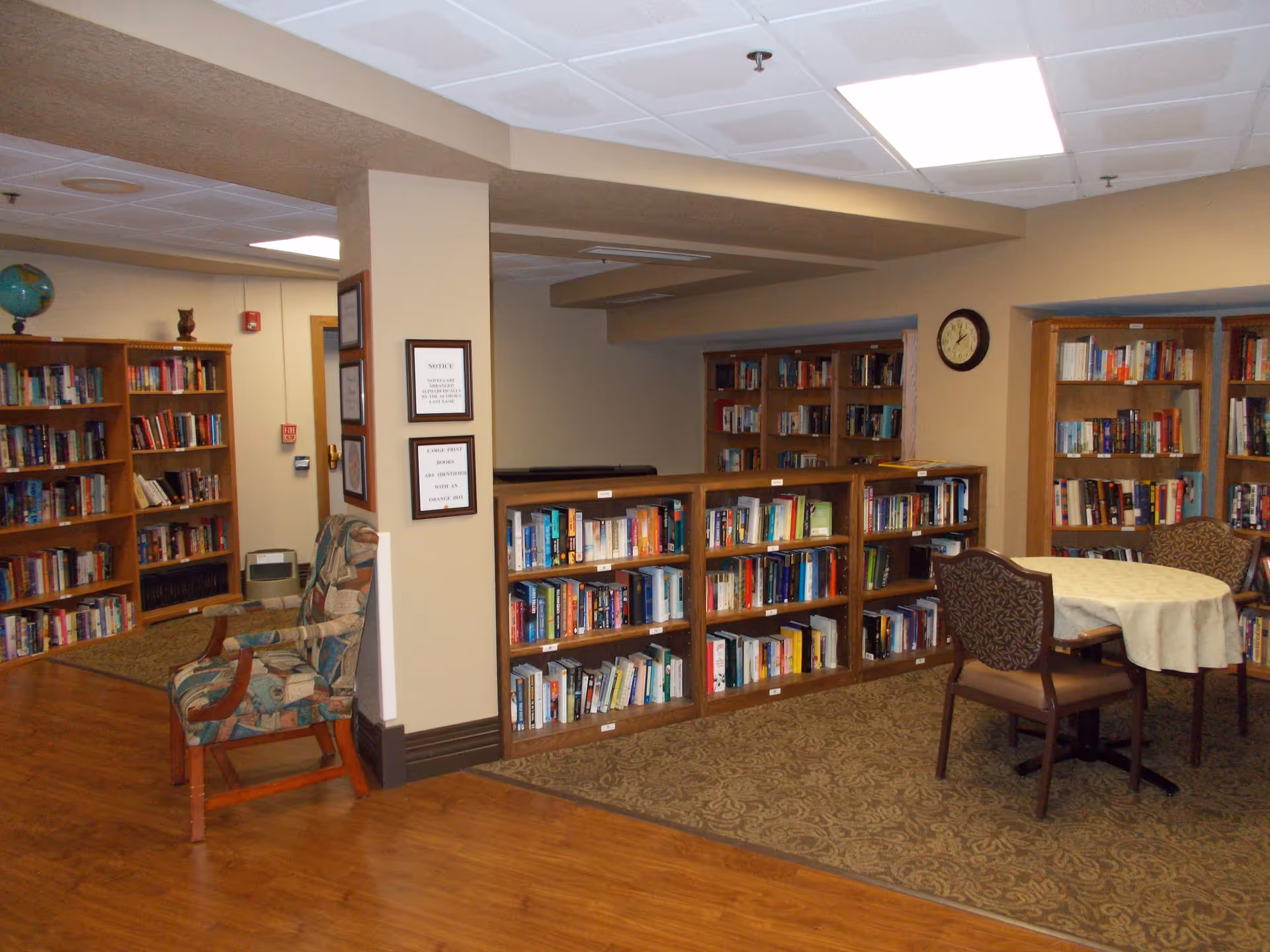 A cozy communal library room with wooden bookshelves, chairs, and a small round table.