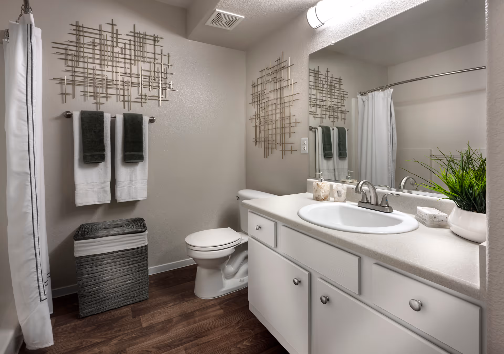 Bright modern bathroom with a sink and countertop, mirror, toilet, shower curtain, towels and decorative wall art.