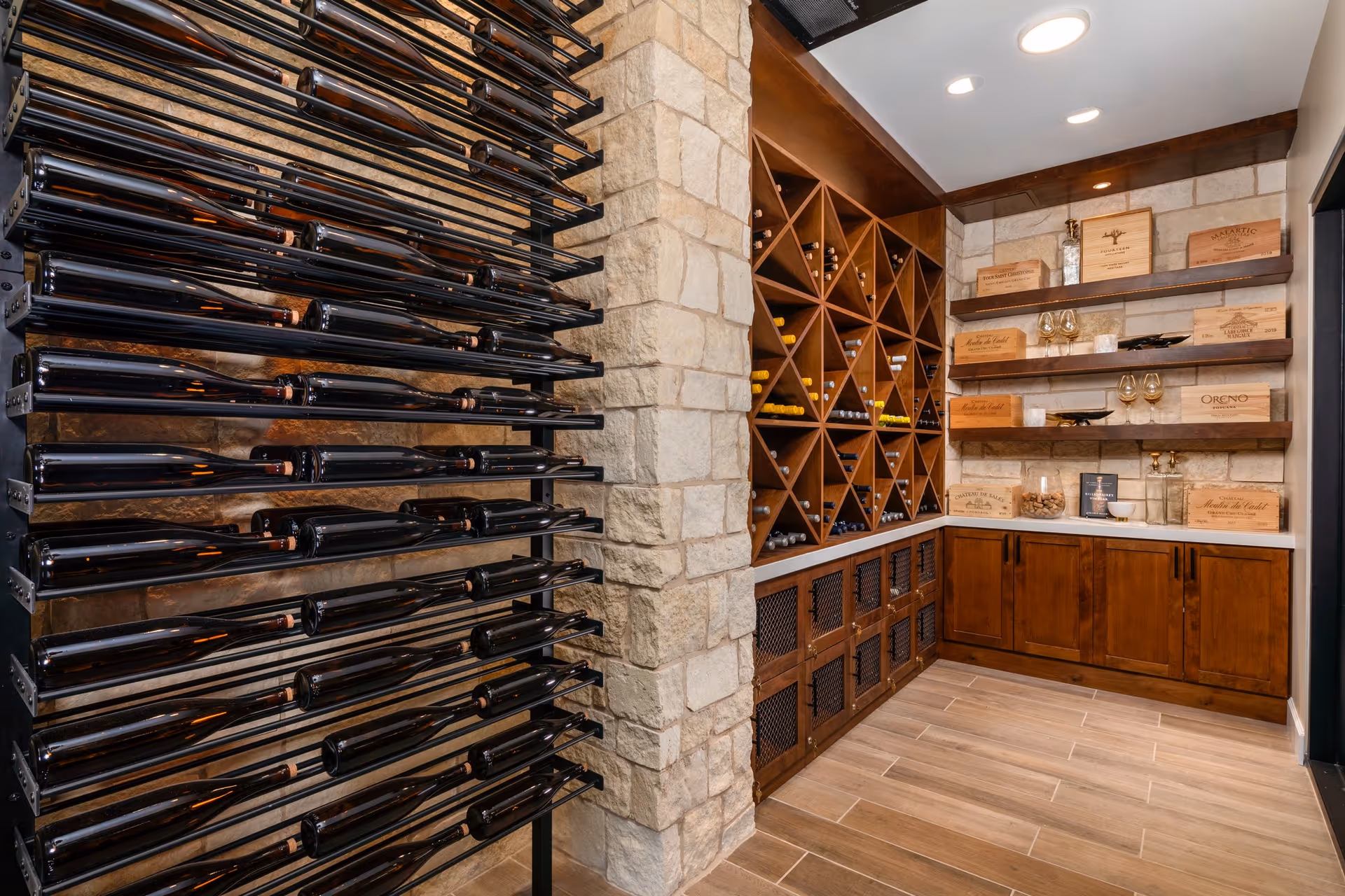 Interior wine storage room with horizontal bottle racks, wooden wine cubbies, shelves of wine boxes and glassware, and stone accent walls.