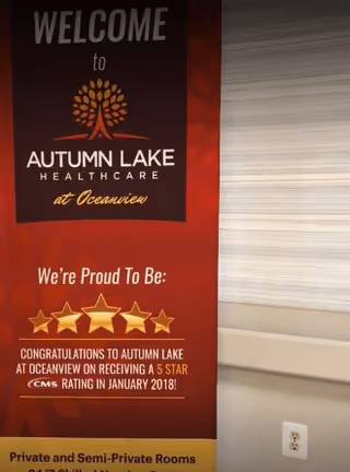 A red and black welcome banner for Autumn Lake Healthcare at Oceanview, highlighting a 5-star CMS rating received in January 2018. The banner features a tree logo and text about private and semi-private rooms, positioned next to a light-colored wall with a power outlet.